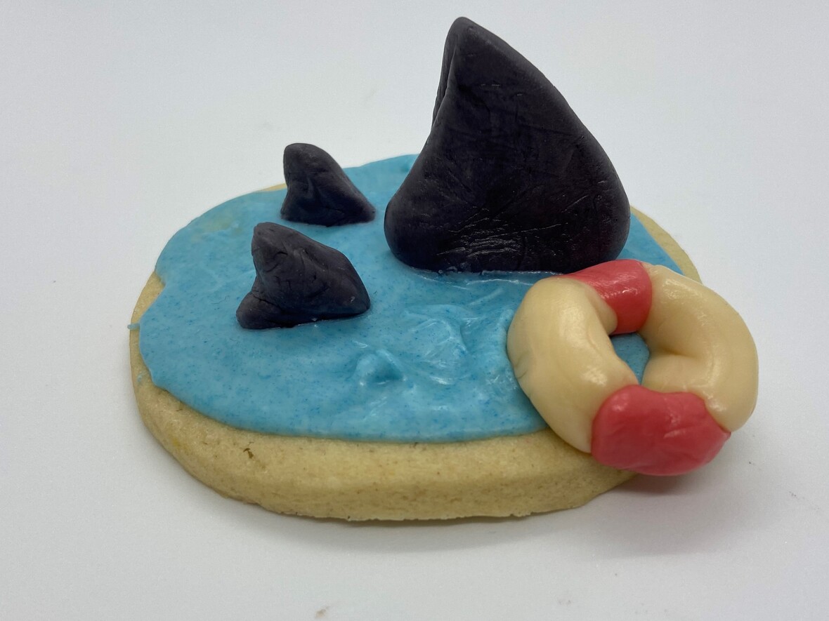 It is a picture of a sugar cookie with blue frosting to look like the ocean. 3 little shark fins are sticking up on the cookie and there is also a little round live perserver.