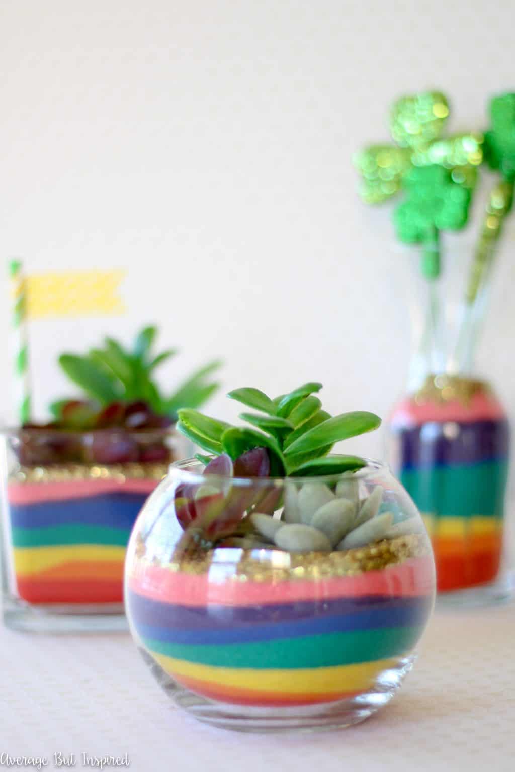 3 small clear glass bowls contains multi-color sand with faux succulent on top.
