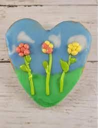 A cookie is a heart shape, with 3 candy made flowers on top of it.