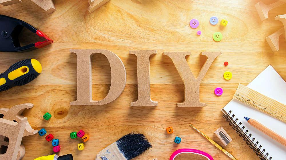 Wooden looking letters spelling out DIY on a table full of tools and craft supplies.