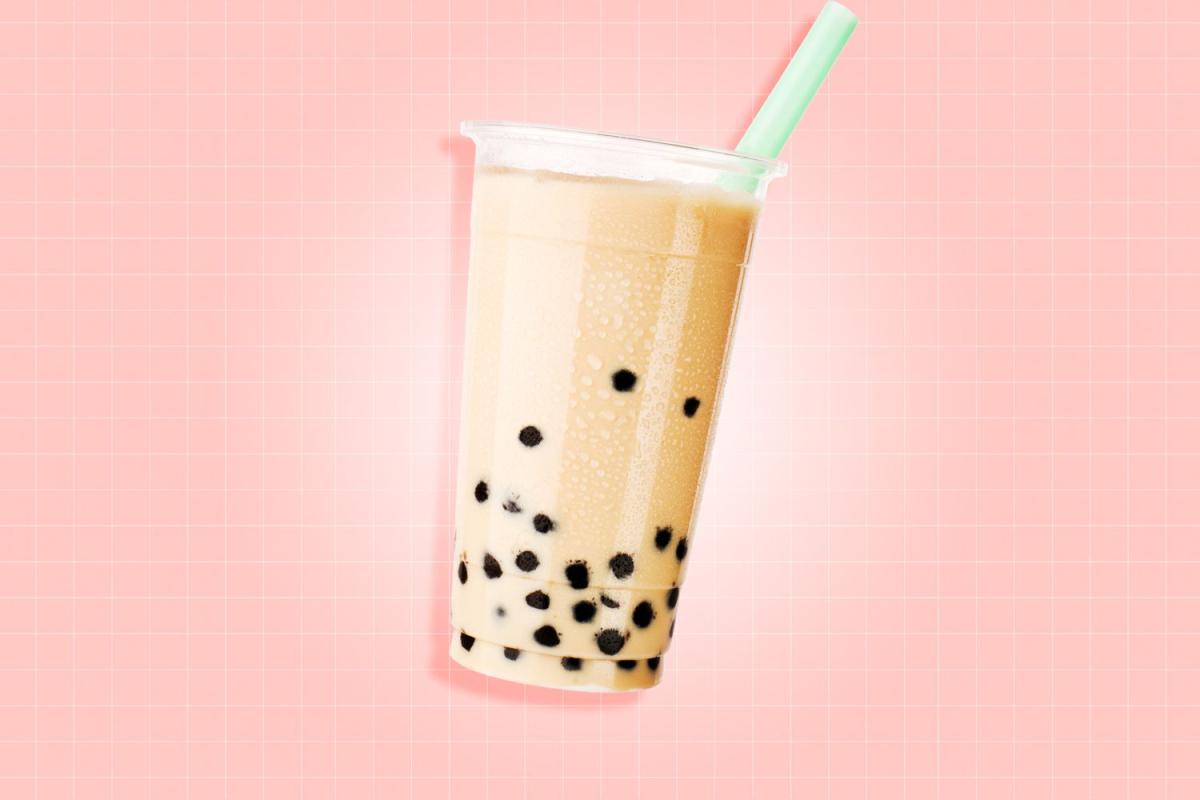 A cup of milk tea with boba in front of a pink background.